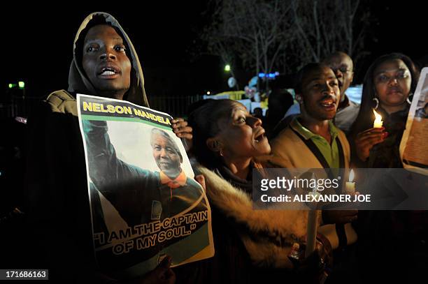 Group of well-wishers hold candles and photos of Nelson Mandela as they pray for his recovery outside the Mediclinic heart hospital where he is...