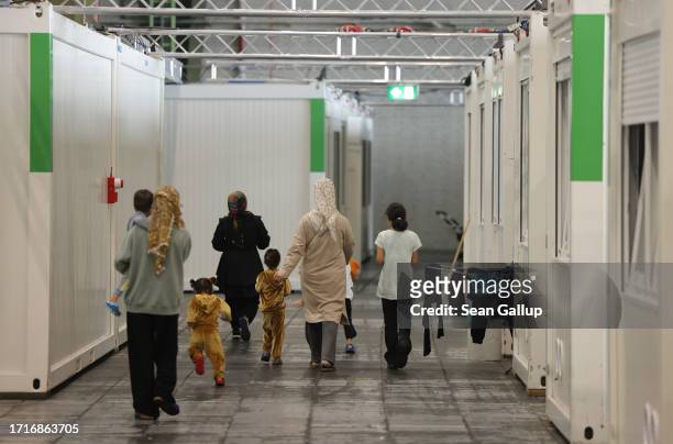 Migrant women and children walk among sleeping quarters containers at a shelter for migrants and refugees inside a hangar at former Tempelhof airport...