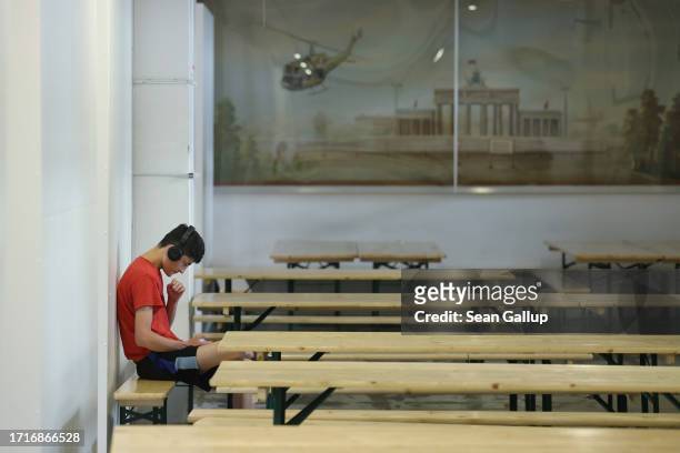 Migrant from Afghanistan plays a game on his smartphone as a picture behind shows the Brandenburg Gate at a shelter for migrants and refugees inside...