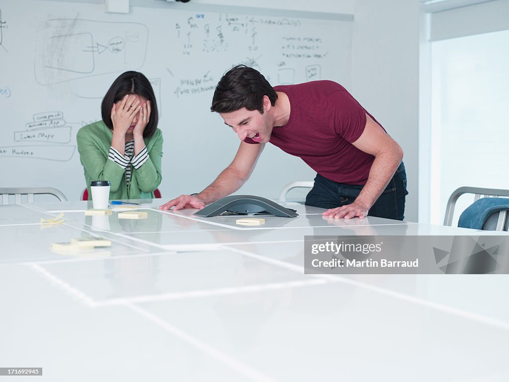 Businesswoman yelling into teleconferencing equipment in conference room