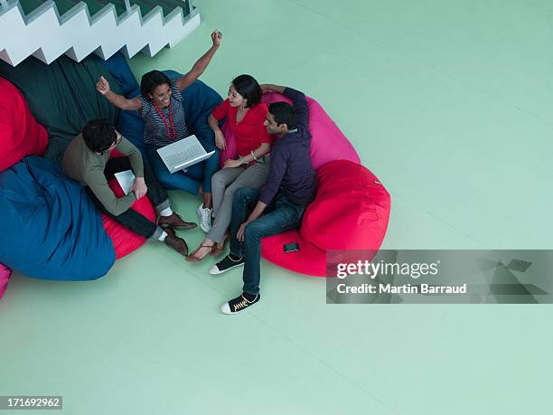excited business people with arms raised sitting in bean bag chairs and looking at laptop - beanbag chair stockfoto's en -beelden