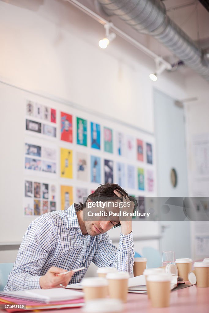 Businessman with head in hands surrounded by coffee cups in office