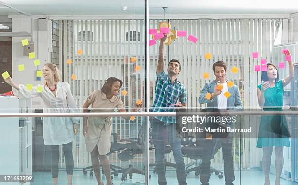 excited business people with arms raised at window covered in adhesive notes - pret stockfoto's en -beelden
