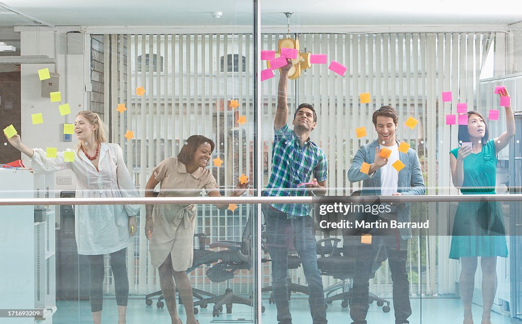 Excited business people with arms raised at window covered in adhesive notes