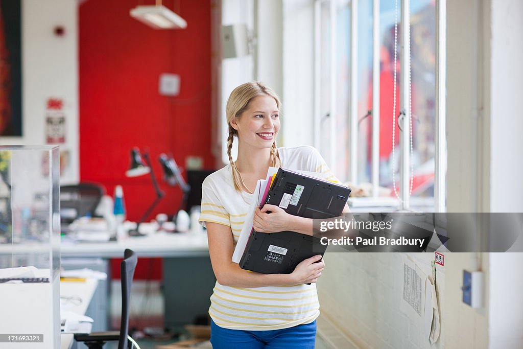 Smiling woman holding laptop and paperwork in office