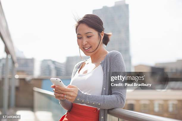 smiling businesswoman text messaging with cell phone on urban balcony - mobile phone reading low angle stock pictures, royalty-free photos & images