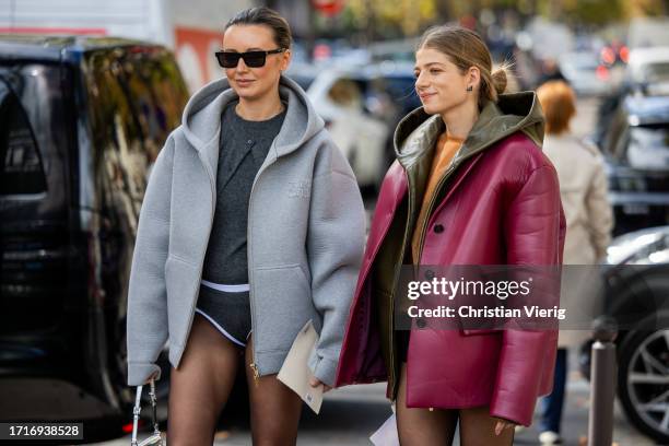 Nataly Osmann wears grey hooded jacket, tights, grey jumper, shorts & a guest wears oversized burgundy leather jacket outside Miu Miu during the...