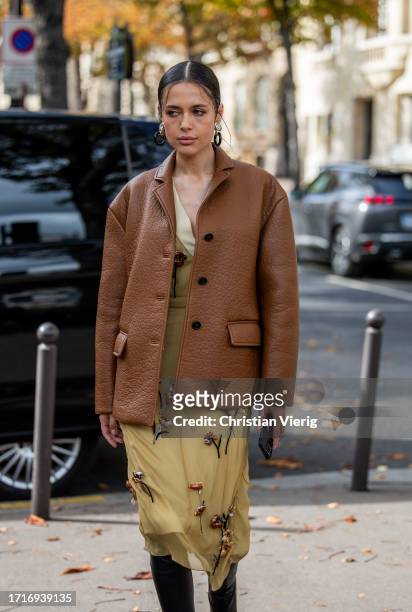 Guest wears brown leather jacket, beige embroidered dress, black boots outside Miu Miu during the Womenswear Spring/Summer 2024 as part of Paris...