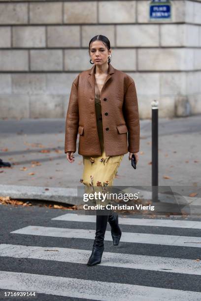 Guest wears brown leather jacket, beige embroidered dress, black boots outside Miu Miu during the Womenswear Spring/Summer 2024 as part of Paris...