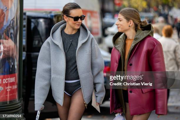 Nataly Osmann wears grey hooded jacket, tights, grey jumper, shorts & a guest wears oversized burgundy leather jacket outside Miu Miu during the...