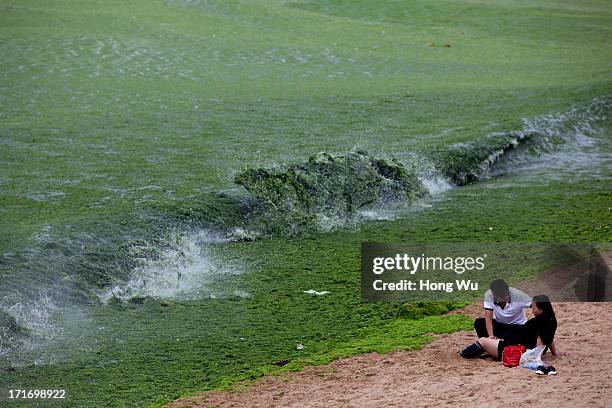 Tourists rests at a beach covered by a thick layer of green algae on June 28, 2013 in Qingdao, China. A large quantity of non-poisonous green...