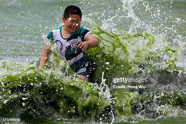 Child plays at a beach covered by a thick layer of green algae on June 28, 2013 in Qingdao, China. A large quantity of non-poisonous green seaweed,...