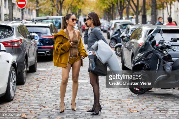 Camila Coelho wears brown transparent top, shorts, brown beige hooded jacket, tights, brown pointed heels & Aimee Song wears grey cardigan, shorts,...