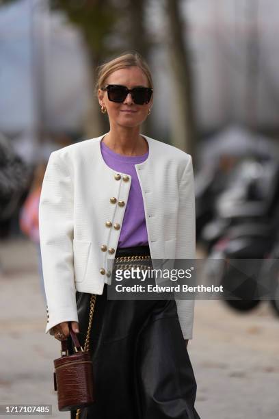 Guest wears sunglasses, a white checked jacket with golden buttons, a purple t-shirt, a black leather skirt, golden chain belt, a brown leather bag...