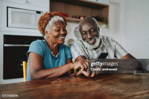 retrato de pareja mayor usando teléfono inteligente en casa - hombres-mayores fotografías e imágenes de stock