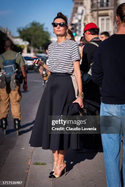 Giovanna Battaglia Engelbert wears a black and grey striped shirt, black midi skirt, nude heels and Dior black bag, outside Sacai, during the...