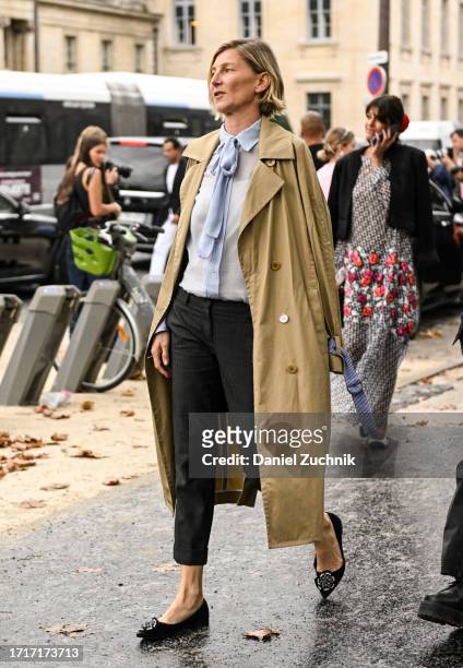 Guest is seen wearing a tan trench coat, blue blouse, black jeans and black flats outside the Chanel show during the Womenswear Spring/Summer 2024 as...