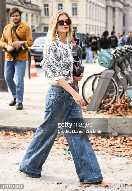 Xenia Adonts is seen wearing a white and silver sequin Chanel top, blue jeans, brown bag and black sunglasses with Chanel earrings outside the Chanel...