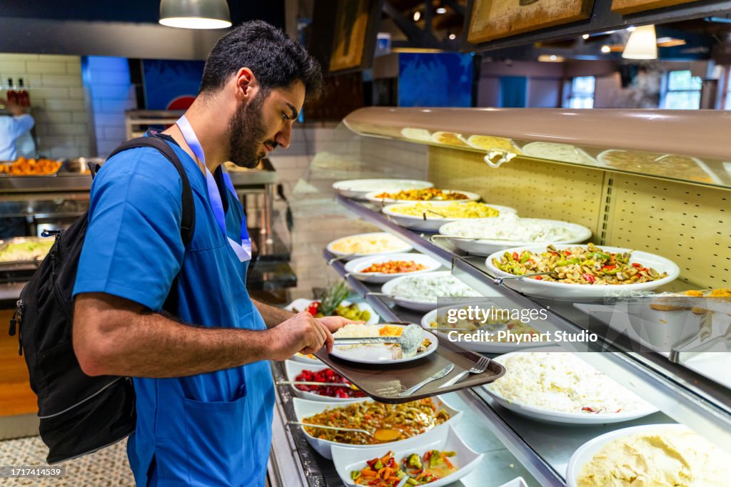 Mann in medizinischen Kitteln isst in einer Cafeteria im Buffetstil