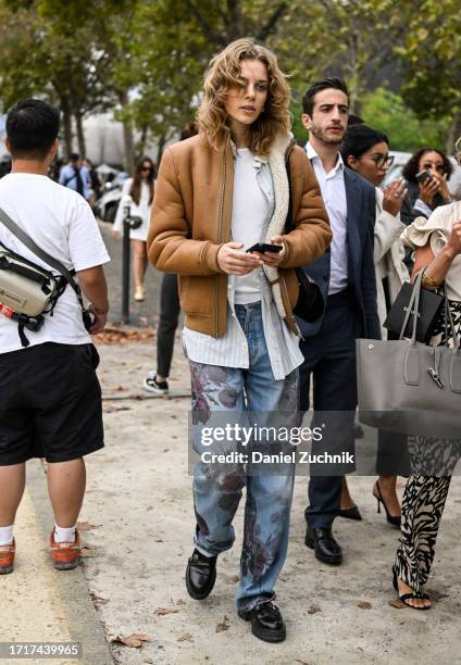 Model Anouk Smits is seen wearing a brown coat, white shirt, blue floral pants and black shoes outside the Chanel show during the Womenswear...