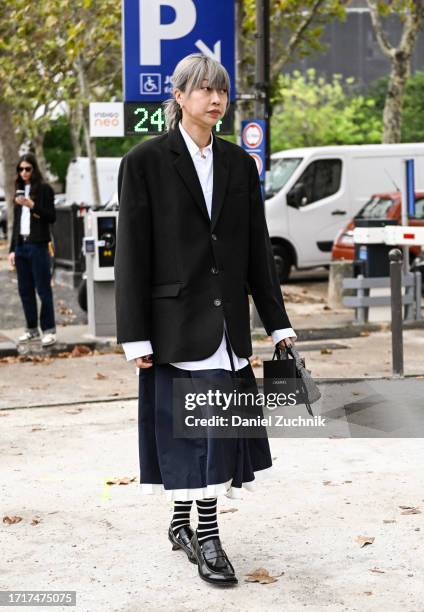 Guest is seen wearing a black jacket, white shirt, black skirt and black shoes with black and white stripe socks outside the Chanel show during the...