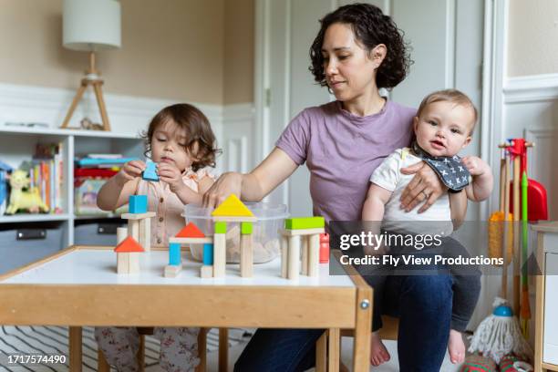 mom and two kids building with wooden block in playroom - baby blocks stock pictures, royalty-free photos & images