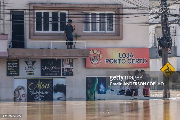 People on a boat talk to a stranded neighbour in the flooded Canoas neighbourhood in Rio do Sul, Santa Catarina State, Brazil, on October 10, 2023....