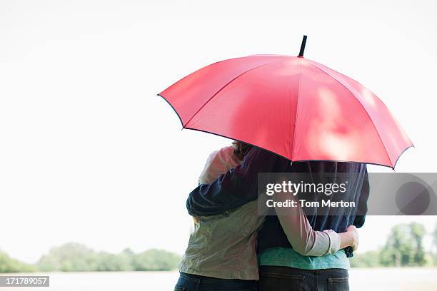 paar umarmen unter roten regenschirm - vorsorge stock-fotos und bilder