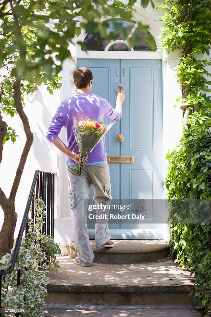 Man holding bouquet of flowers and knocking on door