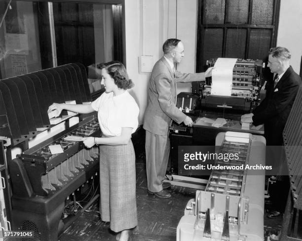 Woman worker loading punch cards and two men viewing a printout from an IBM accounting machine at the Erie Railroad offices, Cleveland, Ohio,...