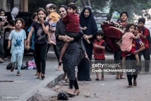 Palestinian women with their children fleeing from their homes following Israeli air strikes rush along a street in Gaza City on October 11, 2023. At...