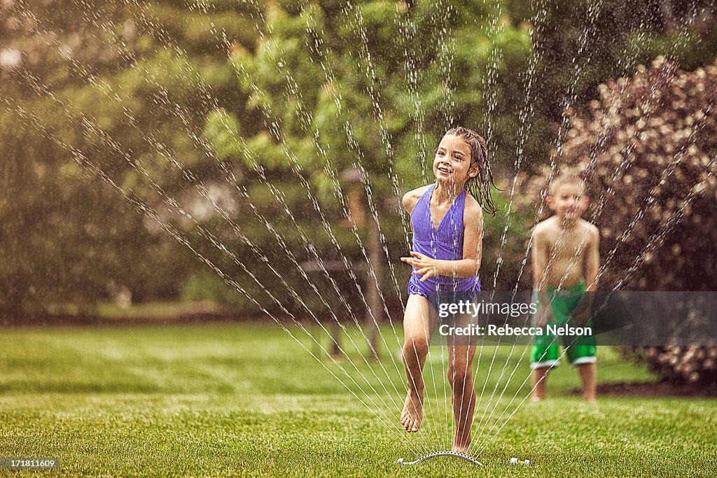 Girl and boy running through garden sprinkler