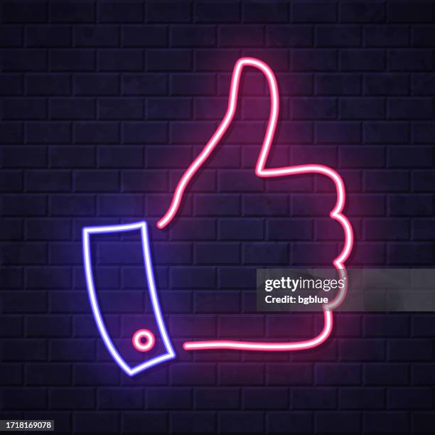 thumbs up. glowing neon icon on brick wall background - neon lighting stock illustrations