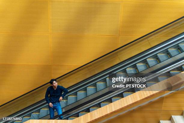 a man wearing glasses stands on the escalator. - airport stairs stock pictures, royalty-free photos & images