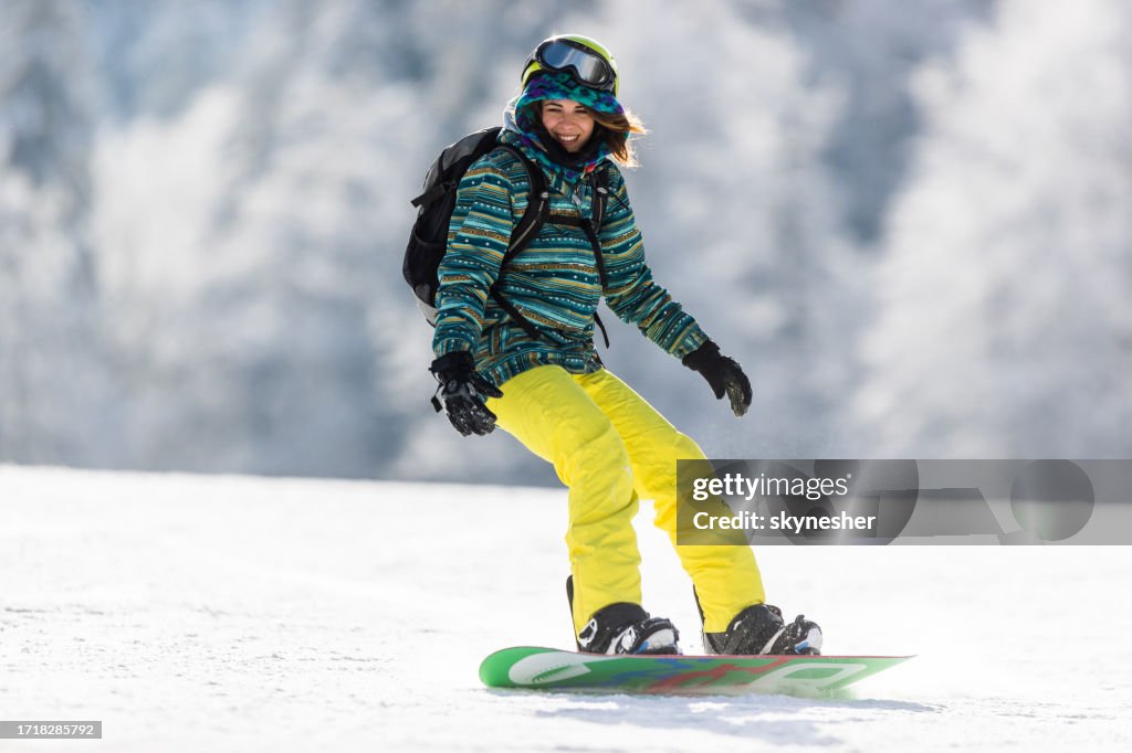 Happy woman snowboarding on a ski slope in winter day.