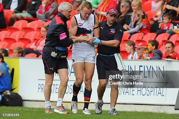 Brent Reilly of the Crows is helped from the field injured during the round 14 AFL match between the Gold Coast Suns and the Adelaide Crows at...