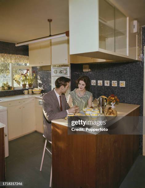 Interior view of a man and woman seated on stools enjoying a breakfast of coffee and croissants in a kitchen diner on the ground floor of a modern...