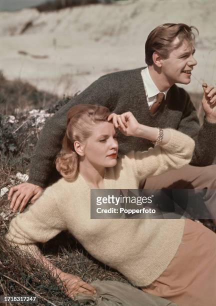 Female fashion model wears a V-necked pullover in cream mohair wool, knitted in stocking stitch with ribbed neck detail, she rests on grass next to a...