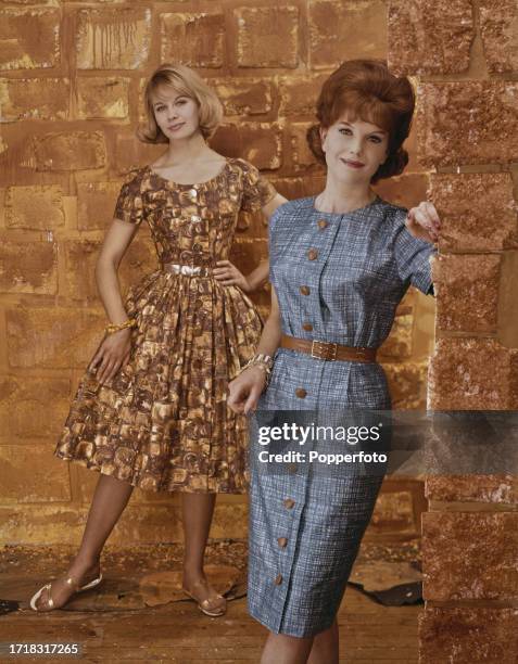 Posed scene of two female fashion models wearing belted button through dresses, the woman on left wears a version incorporating a full skirt in a...