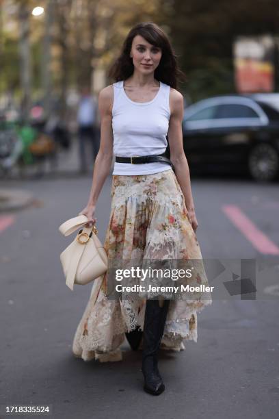 Mary Leest is seen outside Zimmermann show wearing white tank top, black belt above with golden hardware, beige flower lace skirt, vanilla colored...