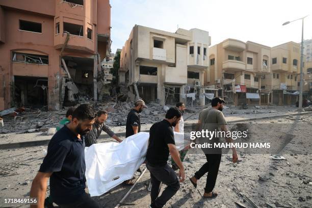 Palestinian men carry away the body of a person killed by Israeli bombardment along a debris-littered street in al-Karama district in Gaza City on...
