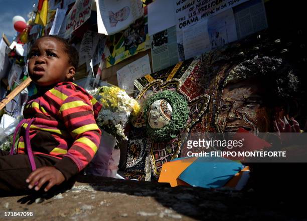 Baby sits by messages and flowers left for former South African President Nelson Mandela outside the MediClinic Heart hospital in Pretoria where...