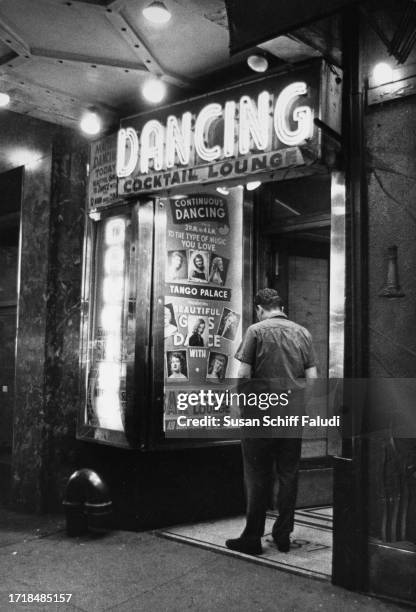 Man stands inspecting portraits of dancers displayed in a glass case at the entrance to a cocktail lounge in Times Square, in Midtown Manhattan, New...