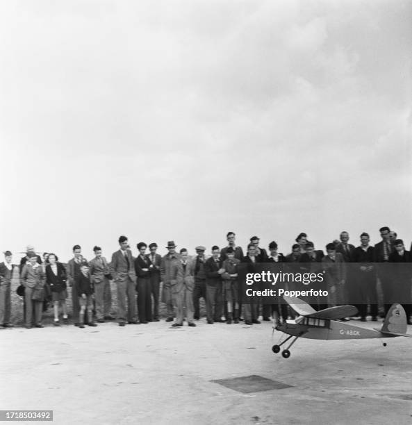 Spectators watch a model aeroplane land on a temporary runway during a model plane makers' club meeting in England in April 1946.