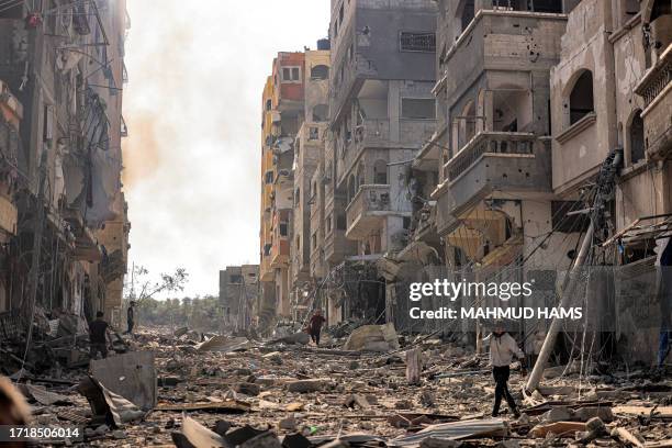 Man carries a propane gas cylinder on his back while walking through debris and destruction littering a street in the Jabalia camp for Palestinian...