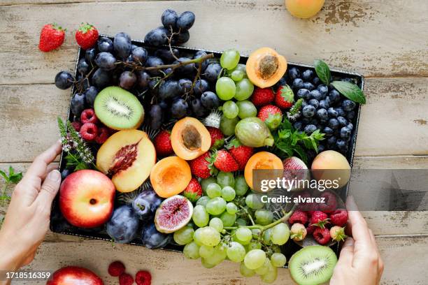 nahaufnahme einer frau, die ein obsttablett auf einem holztisch hält - obstschale stock-fotos und bilder