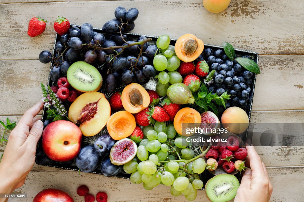 Close-up of a woman hands holding fruit tray on wooden table