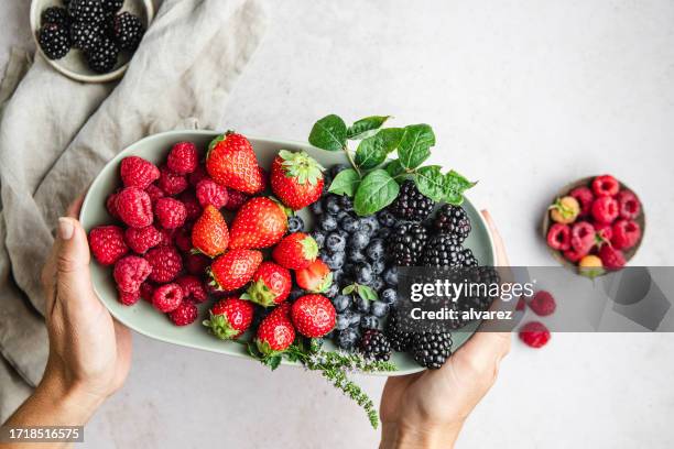 point of view of a woman hands holding plate of berries on white table - blackberry fruit on white stock pictures, royalty-free photos & images