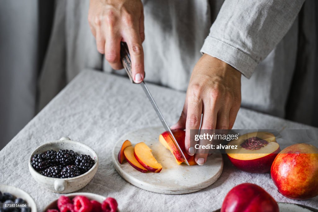 Close-up of a woman preparing fruit salad on kitchen table