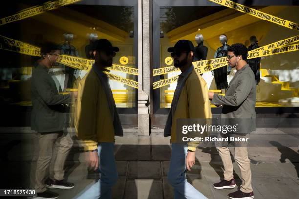 Shoppers and their symmetrical reflections and a window of Selfridges department store on Oxford Street, on 10th October 2023, in London, England.